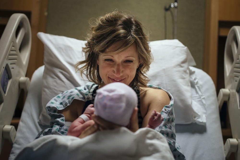 Woman smiling at her newborn baby in a hospital bed.