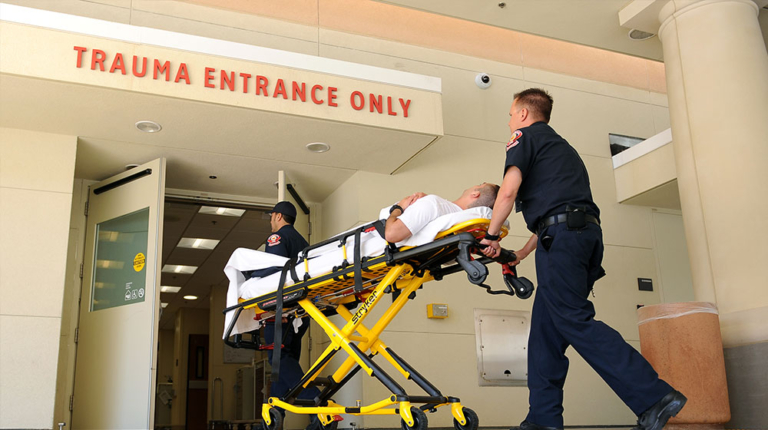 Paramedics wheeling patient through trauma entrance on stretcher.