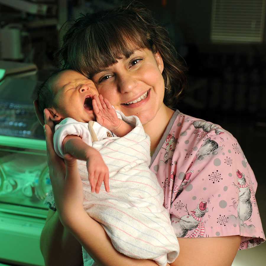 Smiling female maternity nurse holding yawning newborn baby