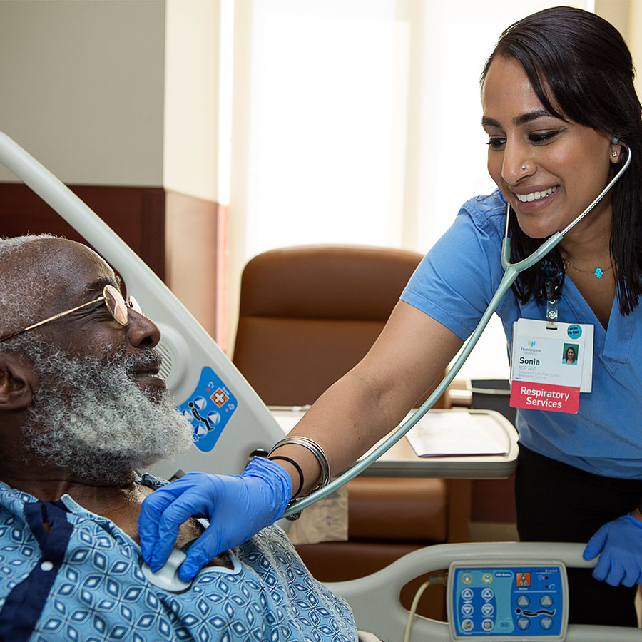 Female smiling nurse checking the heart rate of elderly male patient in hospital bed