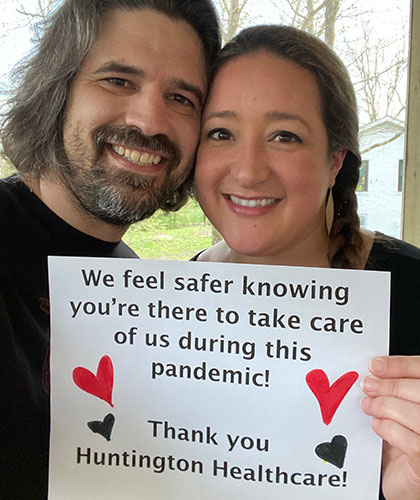 A couple holding a sign that reads We feel safer knowing youre there to take care of us during the pandemic! Thank you Huntington Healthcare!