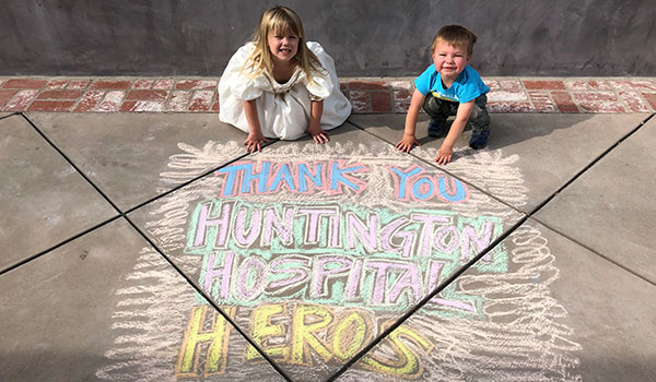 Two children sitting on the ground in back of a chalk drawing saying "Thank you huntington hospital heros"