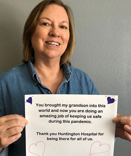 A woman holding a sign that reads You brought my grandson into this world and now you are doing an amazing job of keeping us safe during this pandemic. Thank you Huntington Hospital for being there for all of us.