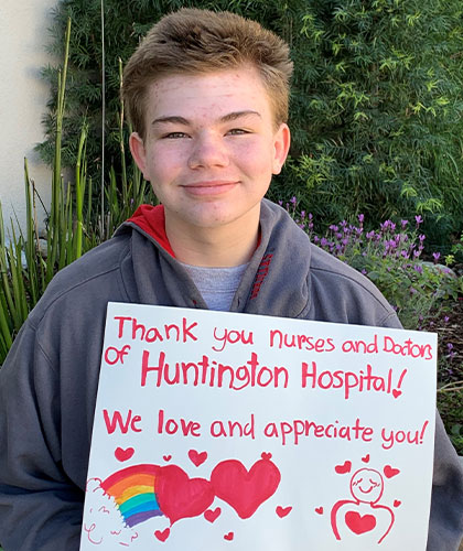 A young man holds a sign that reads Thank you nurses and doctors of Huntingon Hospital! We love and appreciate you!