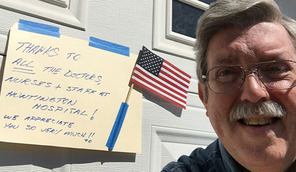 A selfie of an older man. A sign behind him reads Thanks to all the doctors, nurses, and staff at Huntington Hospital! We appreciate you so very much.
