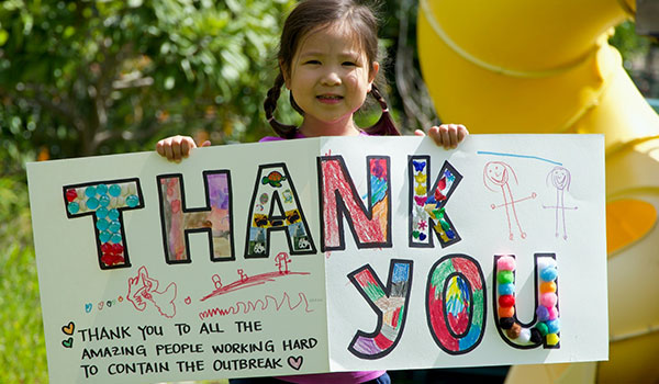 A little girl holds a sign that reads Thank you. Thank you to all the amazing people working hard to contain the outbreak.