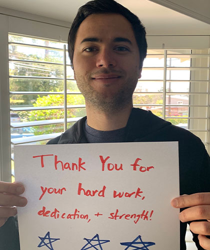 A young man holding a sign that reads Thank you for your hard work, dedication, and strength