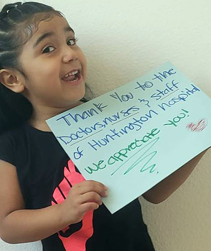 A young girl holds a sign that reads Thank you to the doctors and staff of Huntington Hospital. We appreciate you!
