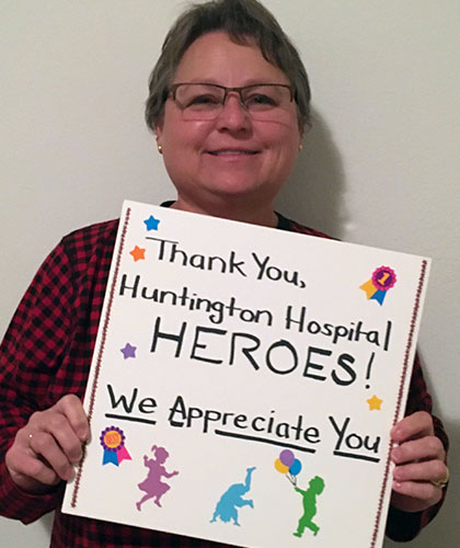 An older woman holds a sign reading Thank you, Huntington Hospital Heroes. We appreciate you