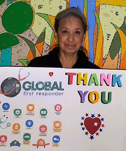 An older woman holds up a sign that reads Thank You Global First Responder