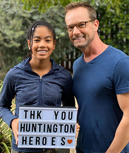 Two smiling people. One holds up a sign that reads Thank you Huntington Heroes