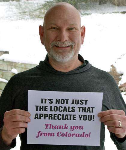 A smiling man holds up a sign that reads Its not just the locals that appreciate you! Thank you from Colorado!
