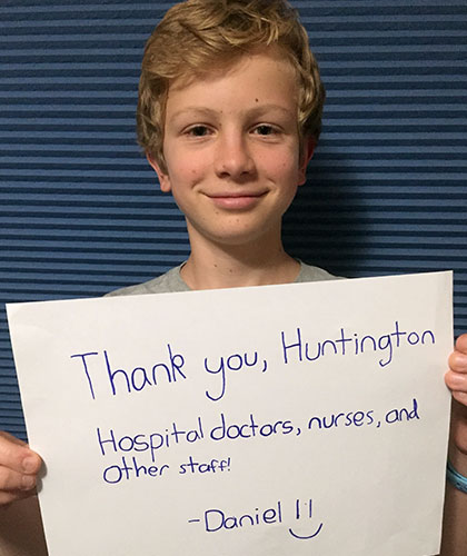 A boy holds up a sign that reads Thank you, Huntington Hospital doctors, nurses, and other staff! From Daniel.