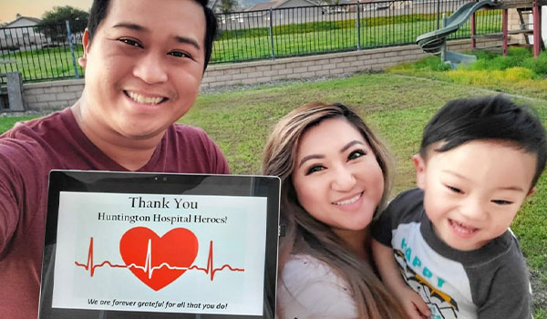 A family consisting of a father, mother and son. The father is holding a tablet with a sign that reads Thak you Huntington Hospital Heroes! We are forever grateful fo all that you do!