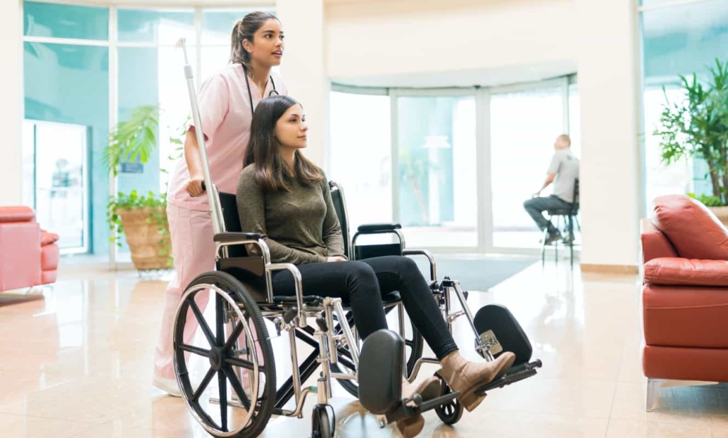 A nurse pushing a wheelchair occupied with a patient.