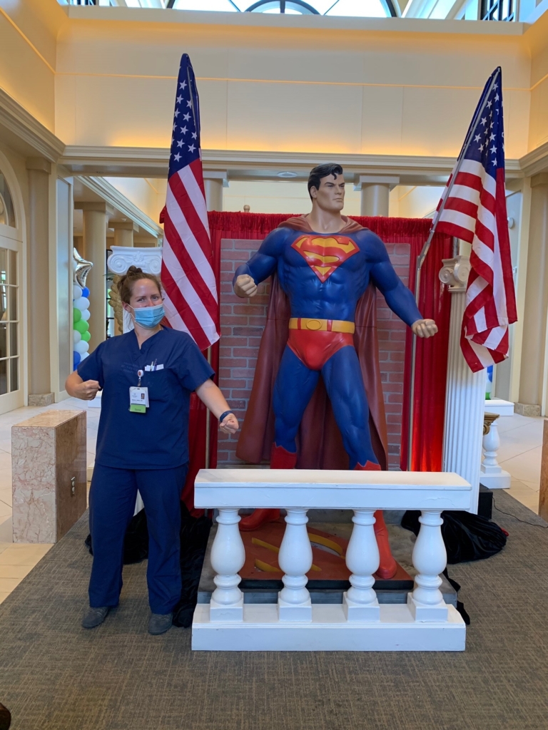 A nurse standing a posing next to a lifesize replica of Superman