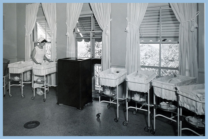 Black and white photo of baby nursery with six babies and one nurse