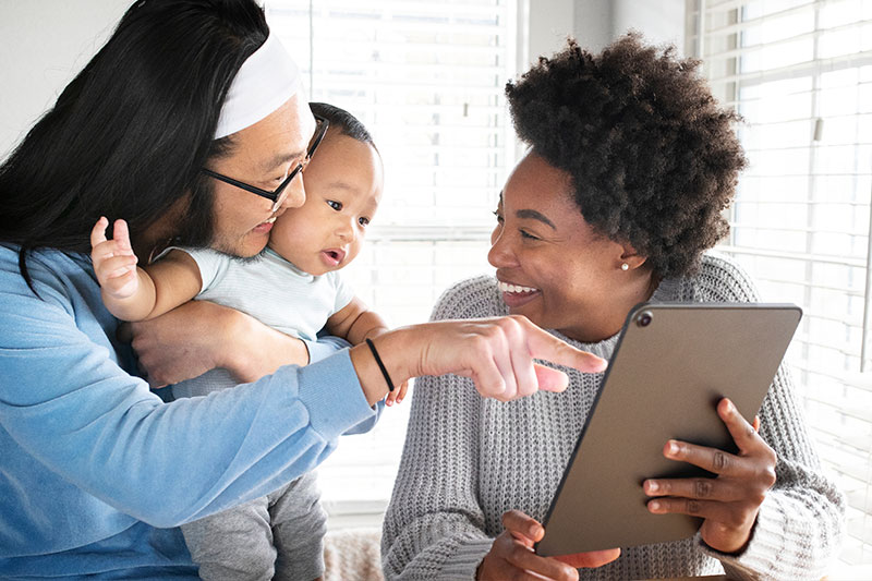 Multi-ethnic couple and baby laughing and pointing to tablet