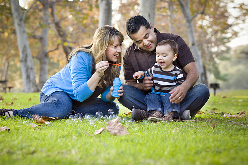 Happy family in the park- mom blows bubbles, child laughs