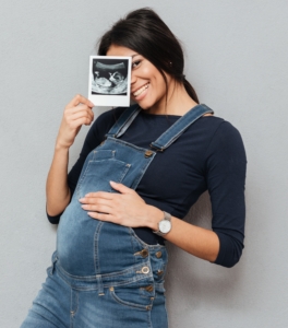 Smiling pregnant woman holds up ultrasound photo.
