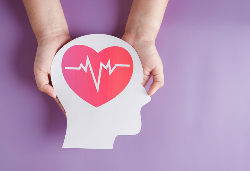 Stroke awareness - hands holding a cardboard cutout of a person's head with a heart and heartbeat graphic near the brain