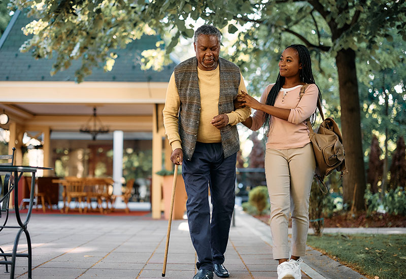 Granddaughter helping her grandfather walk with a cane