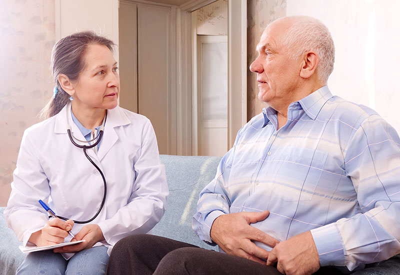 A doctor talking to a senior man who has his hand on his stomach