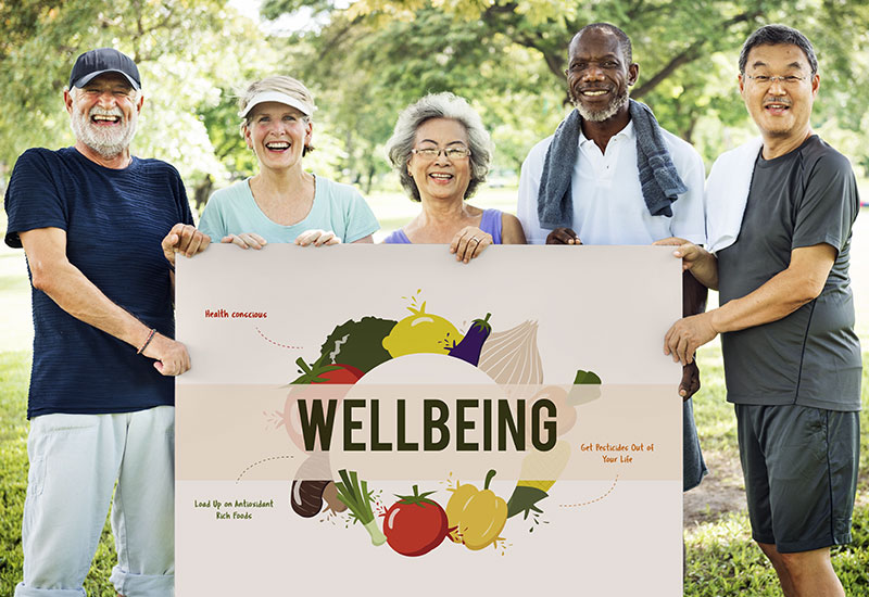 Five seniors holding a sign that says, "wellbeing" with pictures of fruits and vegetables on it
