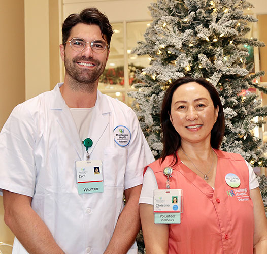 Two Huntington Hospital volunteers standing in front of a christmas tree