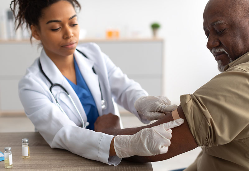 nurse applying a bandaid to a senior man's arm after a vaccination