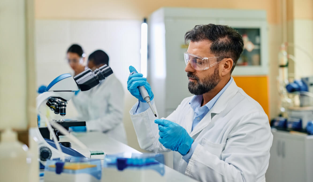Man in lab coat, putting a dropper into a test tube