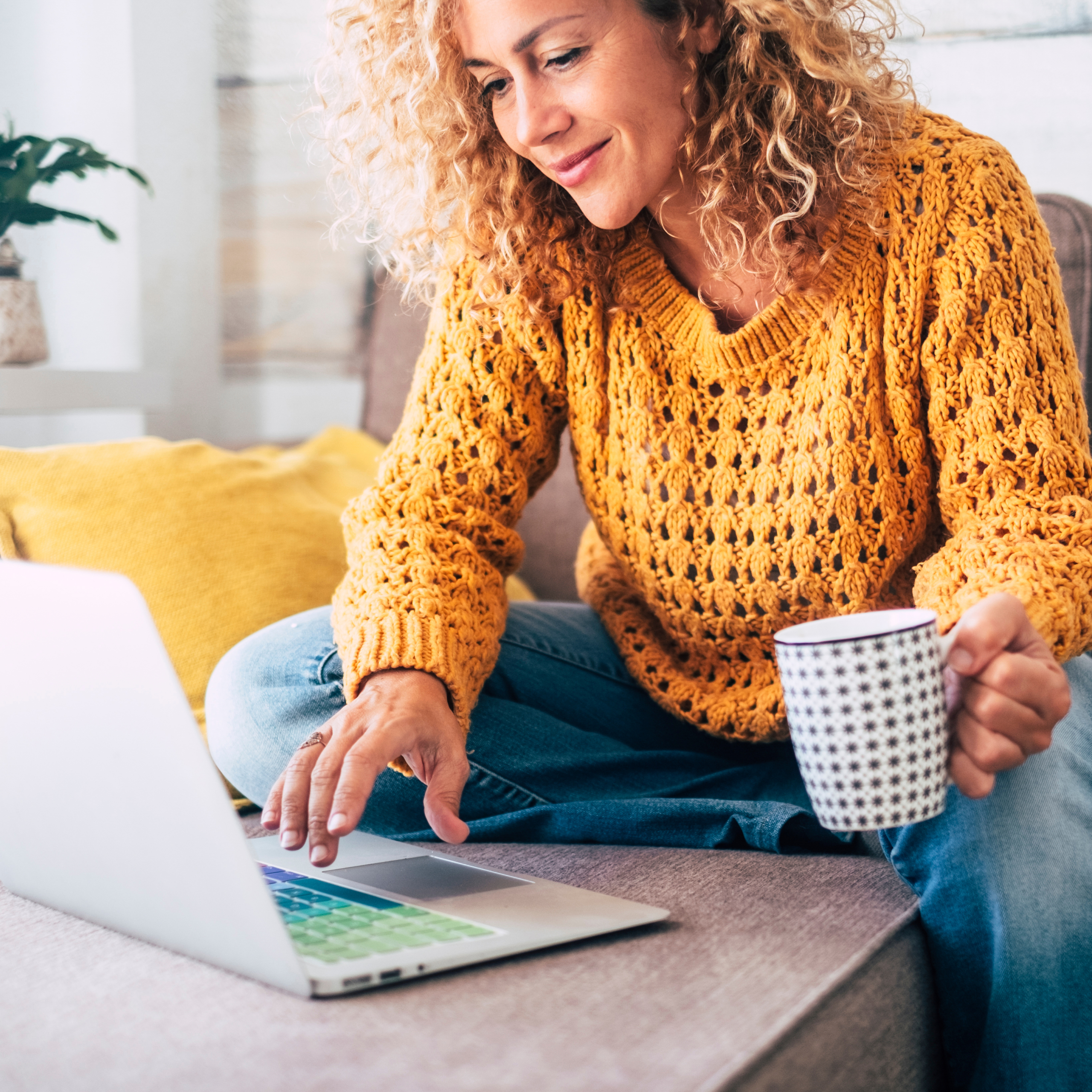Women at desk holding coffee mug and looking at laptop.