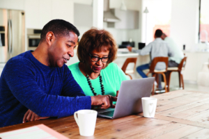 Middle aged black man helping his mother use a laptop computer at home, close up
