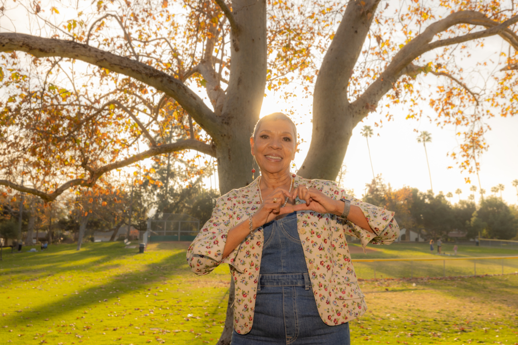 Cardiac patient standing outside making a heart with her hands.