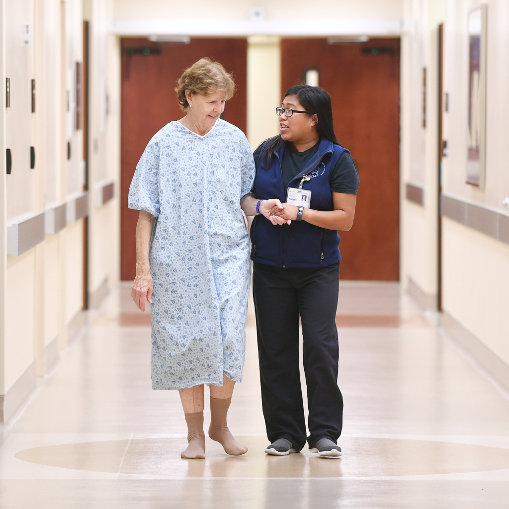 Nurse walking patient down a hospital hallway.