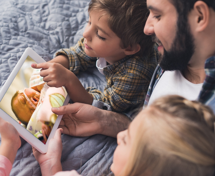 Family members view a newborn receiving care in the NICU through a tablet, demonstrating technology that helps parents and loved ones stay connected to hospitalized infants.